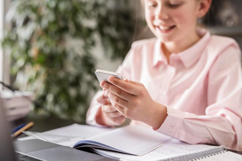 Une élève utilise l'application Mélio sur son téléphone, assise à son bureau avec ses cahiers